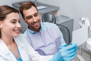 Selective focus of handsome man near attractive dentist smiling in clinic